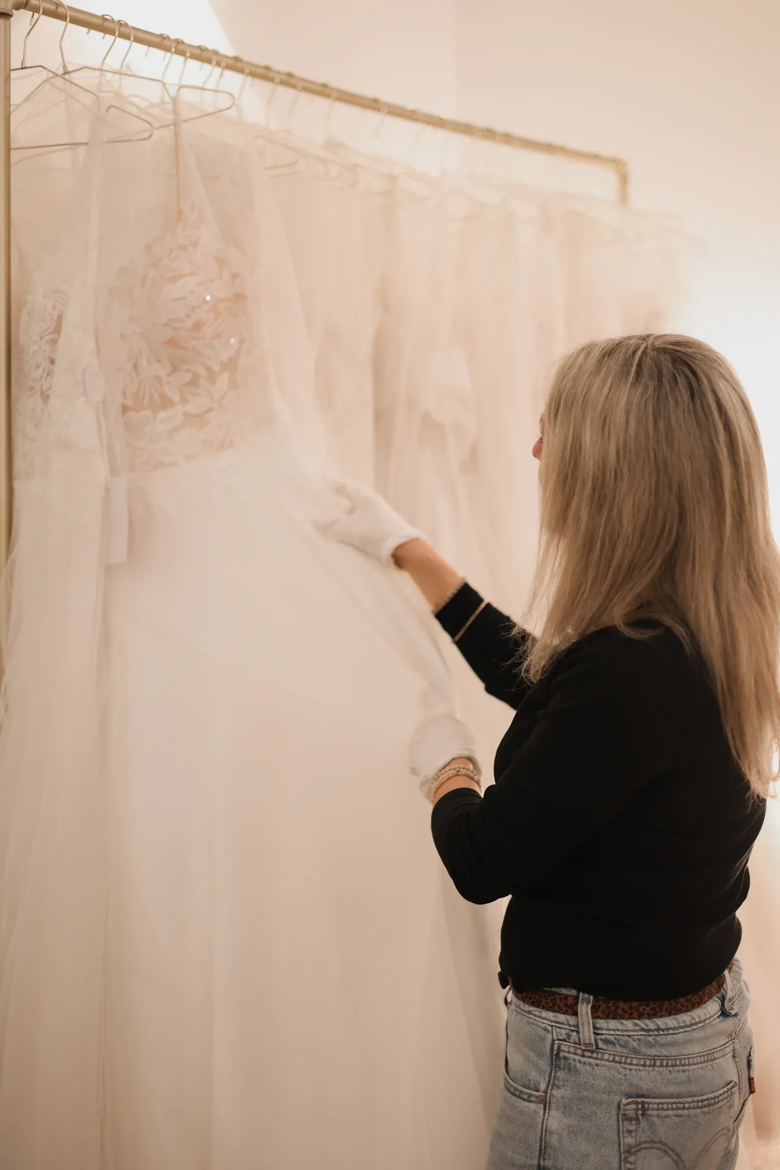 Eine Mitarbeiterin betrachtet ein Brautkleid an der Kleiderstange in der Boutique