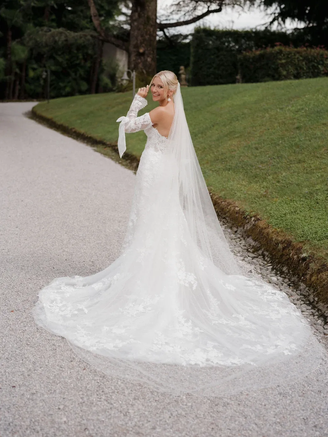 Braut mit langem transparentem Schleier über einem Spitzenkleid im Garten